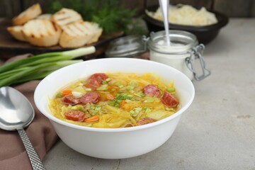 Delicious sauerkraut soup with smoked sausages and green onion served on light grey table