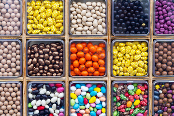 Packaging of multi-colored dragee candies for tasting an assortment of sweets. Gift set of desserts for birthday. Round colored candies covered with bright glaze in wooden boxes. Treats 