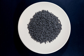 Selective blur on a macro shot of beluga lentils on a grey white plate isolated on a black background. Beluga lentils are black lentils of lens culinaris genus, known for their typical bead shape.