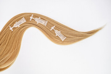 Ampoules for hair growth and restoration, blond hair on a white background. Place for text. Personal care. Morning routine.