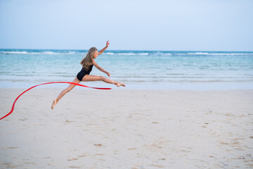 girl gymnast makes an element with a ribbon on the beach, rhythmic gymnastics