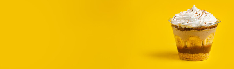 Banoffee pie in a dessert cup (brazilian copo da felicidade - banof, banofe) with yellow background. Ultra wide screen.  Copy space.
