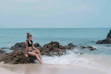 girl sits by the sea on the rocks and enjoys the view, beautiful sea view, children on vacation