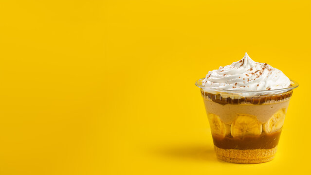 Banoffee pie in a dessert cup (brazilian copo da felicidade - banof, banofe) with banana yellow background. Copy space.