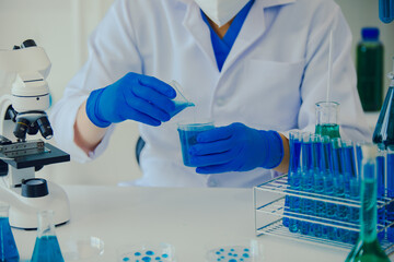medical or scientific researcher researching and experimenting Multi-colored solution, vial and microscope In the laboratory or in the laboratory by wearing blue gloves and white clothing completely.