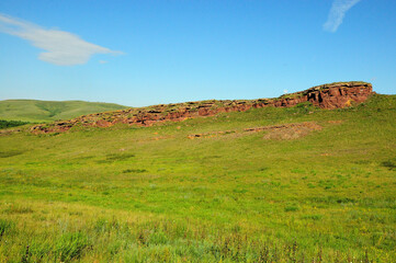 Obraz premium Remains of a ruined ancient red sandstone wall running up the slope to the top of a high gentle hill on a clear summer day.