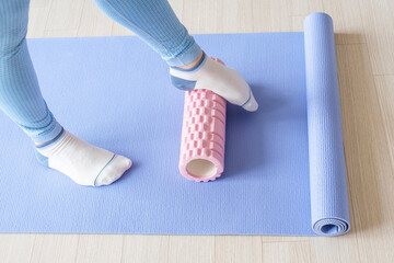 Female foot rolls a massage foam roller close-up on a blue background.