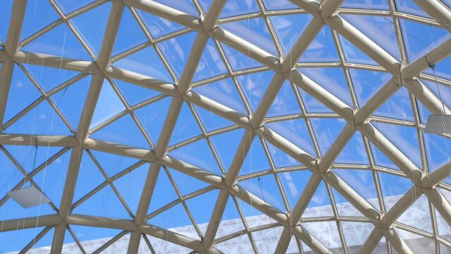 Panorama view of a blue sky through the glass roof of a modern time building with triangular shape of the dome's segments. 4k footage.
