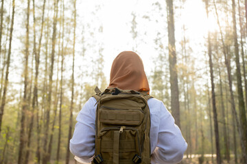 Muslim Asian woman wearing hijab with a backpack and hat hiking in the mountains during the summer season, a traveler walking in the forest. Travel, adventure, and journey concept.