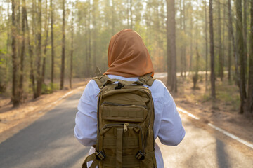 Muslim Asian woman wearing hijab with a backpack and hat hiking in the mountains during the summer...