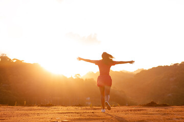 Woman feeling free and happy while running with open arms outdoors with sunset in the background. Gratitude and happiness