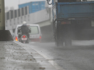 雨の日に水しぶきをあげて走るトラックと前を走るスクーター