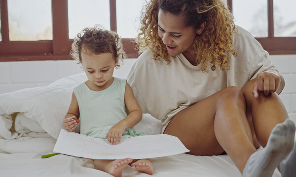 Young mother sitting on bed and drawing with her baby daughter.