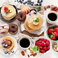 Pancakes with fresh fruits, donuts and coffee on a white background.