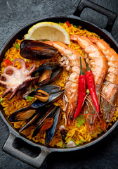 Traditional spanish seafood paella in the fry pan on a black background.