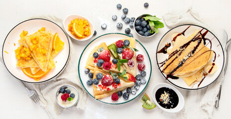 Sweet crepes assortment with berries chocolate on gray background. Homemade food concept. Top view, flat lay