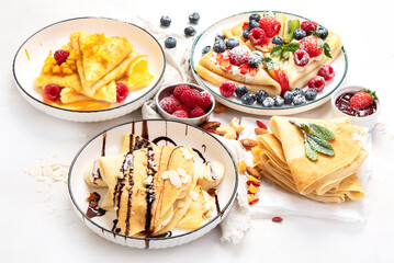 Sweet crepes assortment with berries chocolate on gray background. Homemade food concept. Top view, flat lay