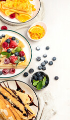 Sweet crepes assortment with berries chocolate on gray background. Homemade food concept. Top view, flat lay