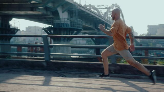 Young sportive man running fast along the street, training outdoors in the city on summer day. Zoom shot, shaky camera