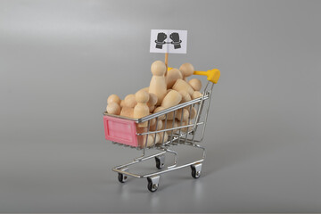 A bunch of wooden figures loaded in a shopping cart represent the concept of human trafficking or...