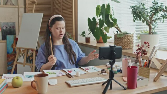 Young woman with Down syndrome working as teacher giving online lesson using smartphone