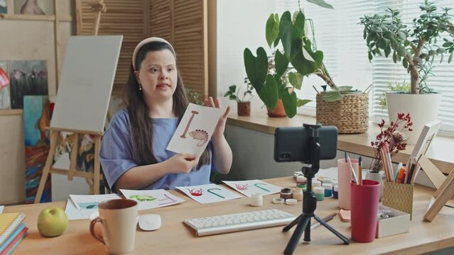 Panning shot of modern teacher of English with Down syndrome working online or recording educational video using smartphone