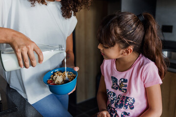 Latin single mother and daughter eating milk and cereal for breakfast at kitchen in Mexico Latin...
