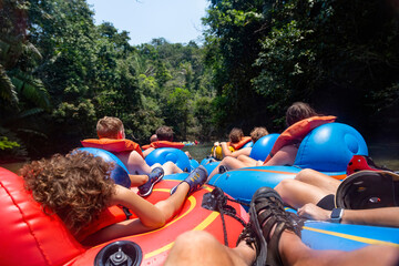 Large group of people floating down a scenic jungle river in Belize Central America on a natural Cave Tubing adventure. Real people having real outdoor fun in the jungle. View from behind - Powered by Adobe
