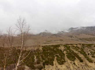 Panorama of mountainous terrain and peaks with low clouds, weather conditions before rain.