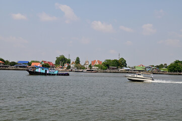 BANGKOK, THAILAND - May 6, 2023 : A small boat is dragging a sand barge through the Chao Phraya...