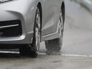 雨の日に濡れた路面を走ってくる乗用車
