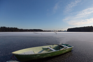 Fototapeta premium A boat stuck in the ice of a forest lake during winter, illuminated by the harsh daylight amidst freezing temperatures.