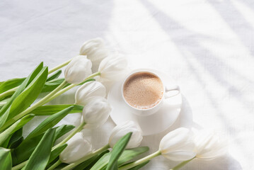 Obraz na płótnie Canvas Cozy morning coffee cup with white tulip flowers from above, breakfast on Mothers day or Womens day. Top view with copy space Floral composition Romantic background