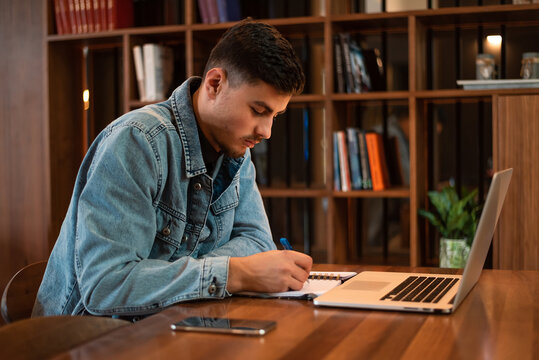 A male college student sitting at the table doing assignments in a university library.