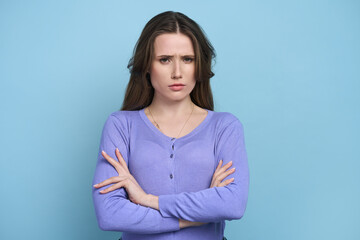 Isolated portrait on blue background of perplexed confuded woman with arms folded