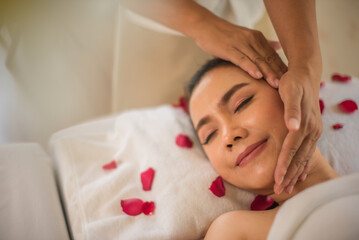 Obraz na płótnie Canvas Beautiful asian client relaxes after a head massage from a professional masseuse on a bed sprinkled with roses in a spa room.