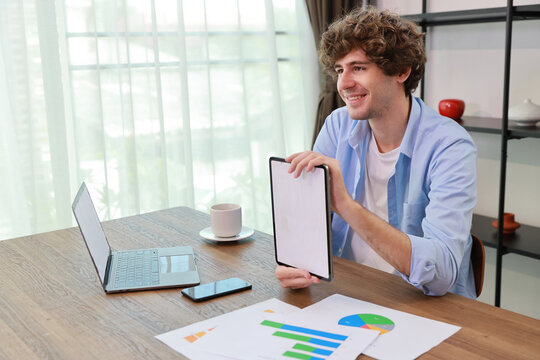 Caucasian businessman online meeting with colleage or customer and showing something on white screen tablet while sitting at home and working