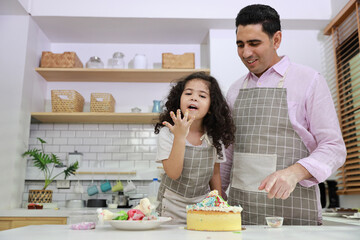 Happy lovely asian single dad and cute daughter in apron having fun with teaching and decorating homemade cake in the kitchen. Family lifestyle cooking with education concept.