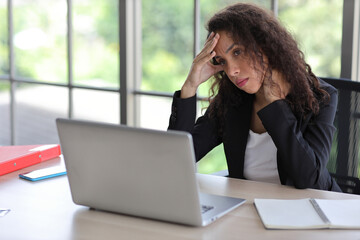 Mid adult businesswoman touching her head on table in office after bad news business failure or get fired and feeling discouraged, distraught and hopeless in modern office.