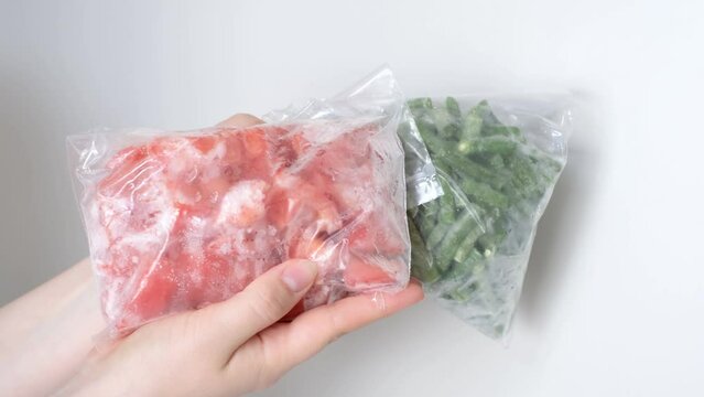 Female hands hold packages of frozen tomatoes and and string beans on white background.
