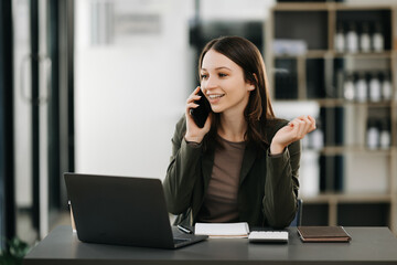 Business Caucasian woman Talking on the phone and using a laptop with a smile while sitting at modern office