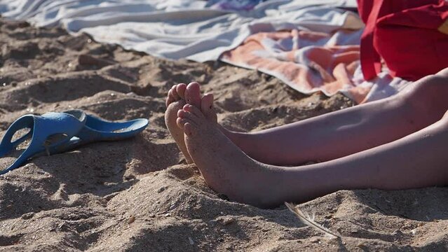 Bare feet of women sitting on sandy beach sunbathing. Wide shot view