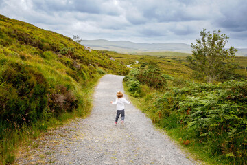 Cute little happy toddler girl running on nature path in Connemara national park in Ireland. Smiling and laughing baby child having fun spending family vacations in nature. Traveling with small kids