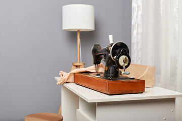 Tailor's workplace with sewing machine and clothing on table in atelier, tailoring workshop, empty space for advertisement.