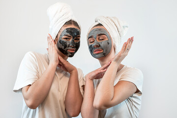 Two caucasian women wear towel having black clay facial mask isolated on white