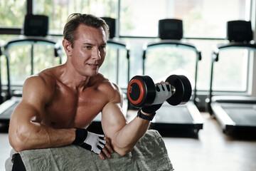Fototapeta na wymiar Smiling middle-aged man working out with heavy dumbbells, upper body workout concept