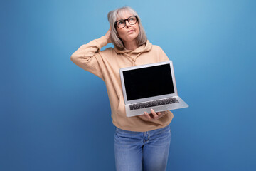 60s mature woman freelancer with gray hair studying remote profession holding laptop in hands on studio background with copy space
