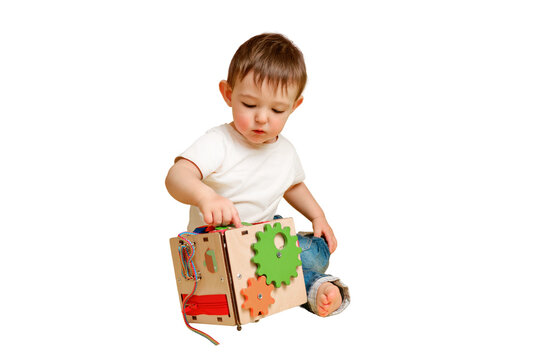 Toddler baby is playing logic educational games busyboard on a studio isolated on a white background. Happy child play with educational toy, learning logic. Kid aged one year four months