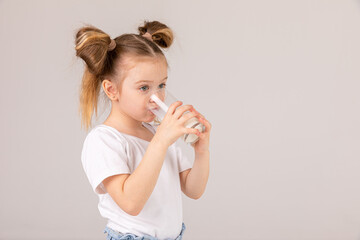 little blonde girl in white tank top drinking milk on a light background, space for text