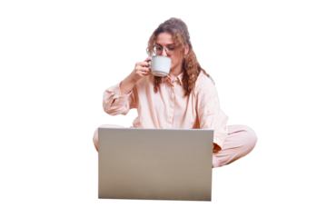 Cute woman drinks coffee on the home bed, isolated on a white background. Redhead woman with a computer working remotely during isolation due to quarantine